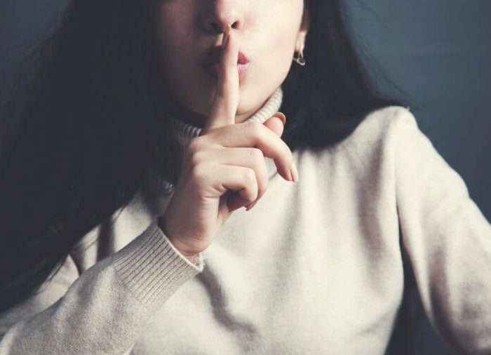 close up of young woman holding finger on lips