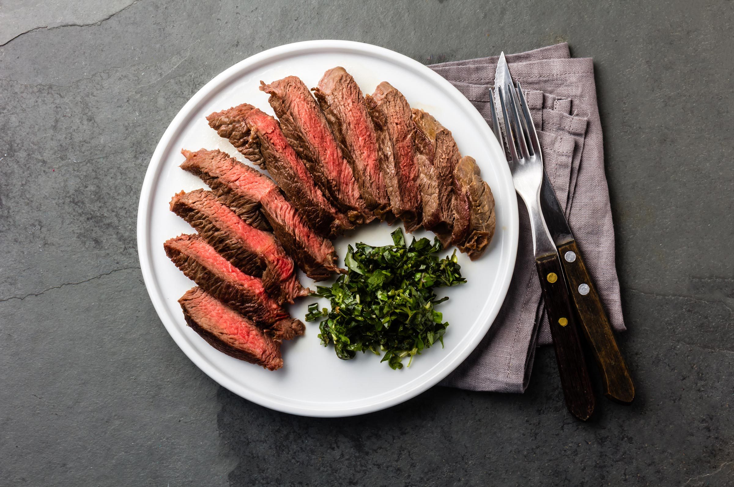 Medium rare sliced beef served on white with herb sauce and vintage cutlery set. Sliced medium rare roast beef on slate gray background