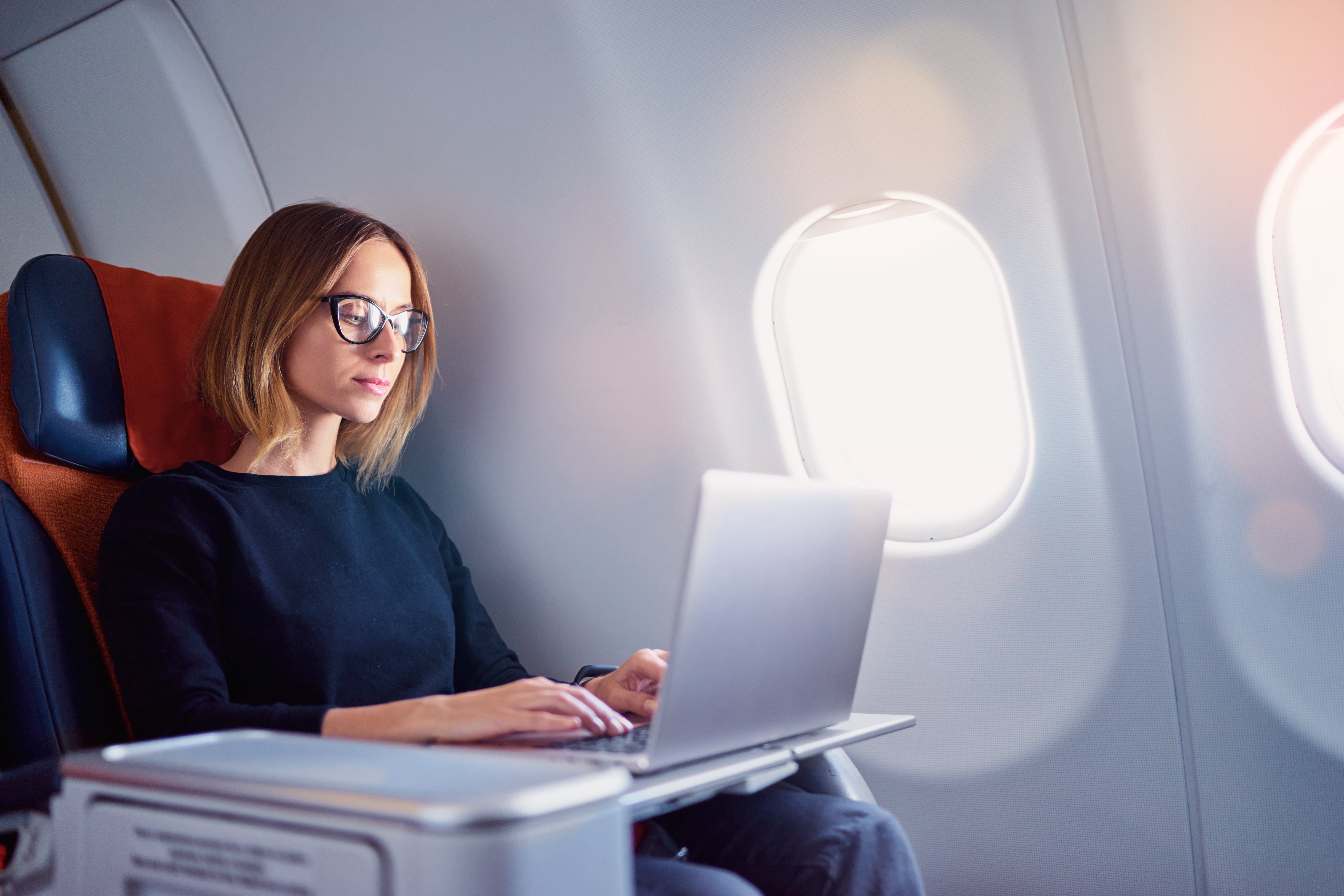 Traveling and technology. Flying at first class. Pretty young businees woman working on laptop computer while sitting in airplane.