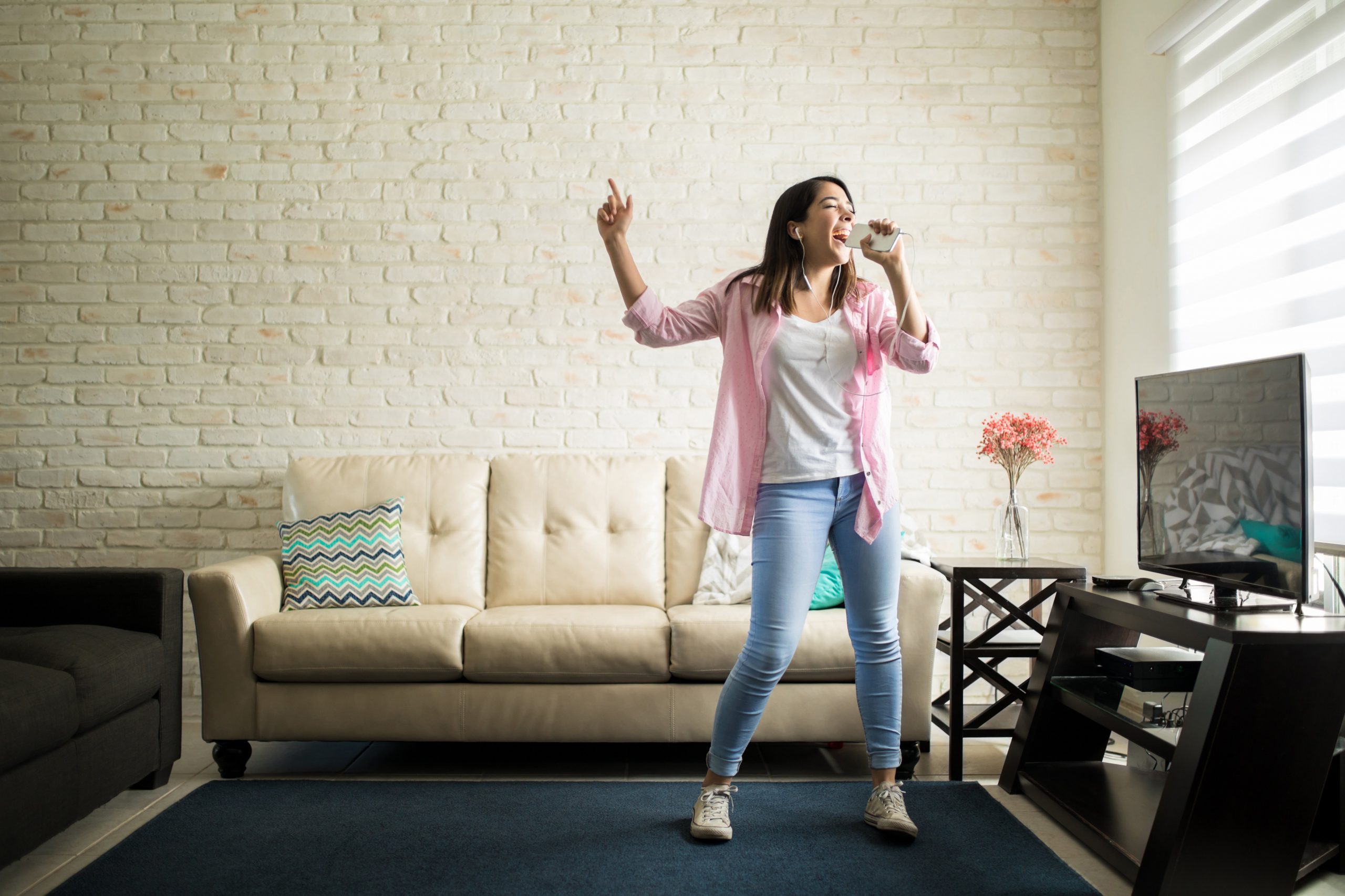 Independent woman singing karaoke alone in her apartment and having fun in the living room